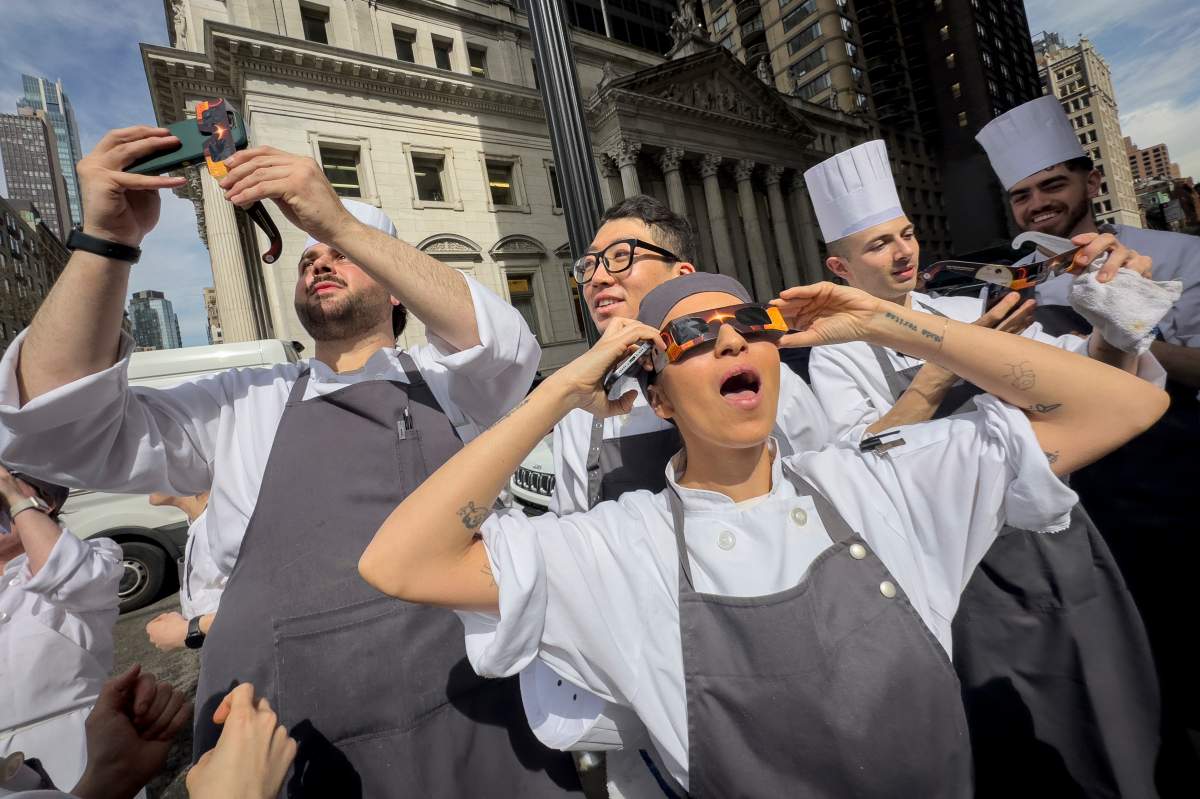 Restaurant workers in the Flatiron district of Manhattan take a break to view the solar eclipse, Monday, April 8, 2024, in New York. (AP Photo/John Minchillo)