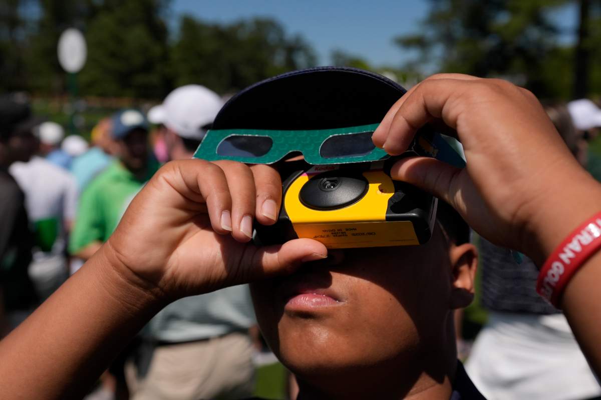 Xeve Perez looks up as the sun during an solar solar eclipse during a practice round in preparation for the Masters golf tournament at Augusta National Golf Club Monday, April 8, 2024, in Augusta, Ga. (AP Photo/George Walker IV)