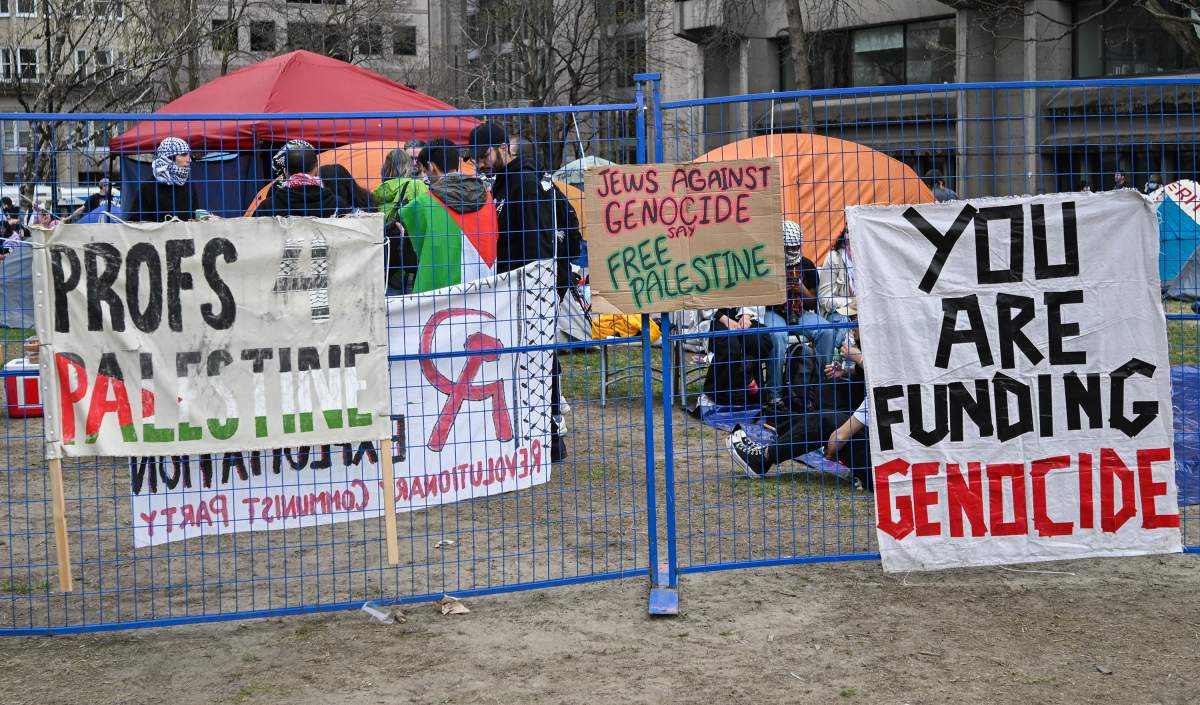 Signs and banners are shown attached to a fence next to a pro-Palestinian demonstration at an encampment at McGill University in Montreal, Saturday, April 27, 2024.