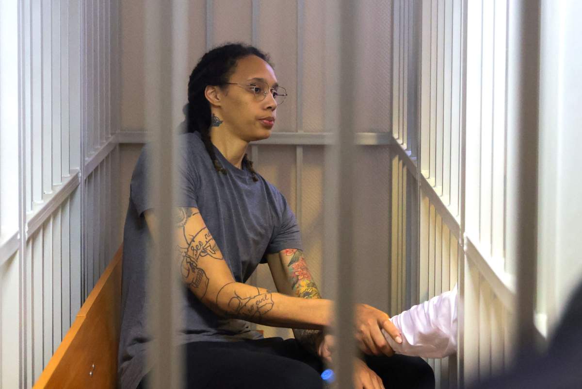 Brittney Griner in a prison cell. She is wearing a grey tee and holding papers.