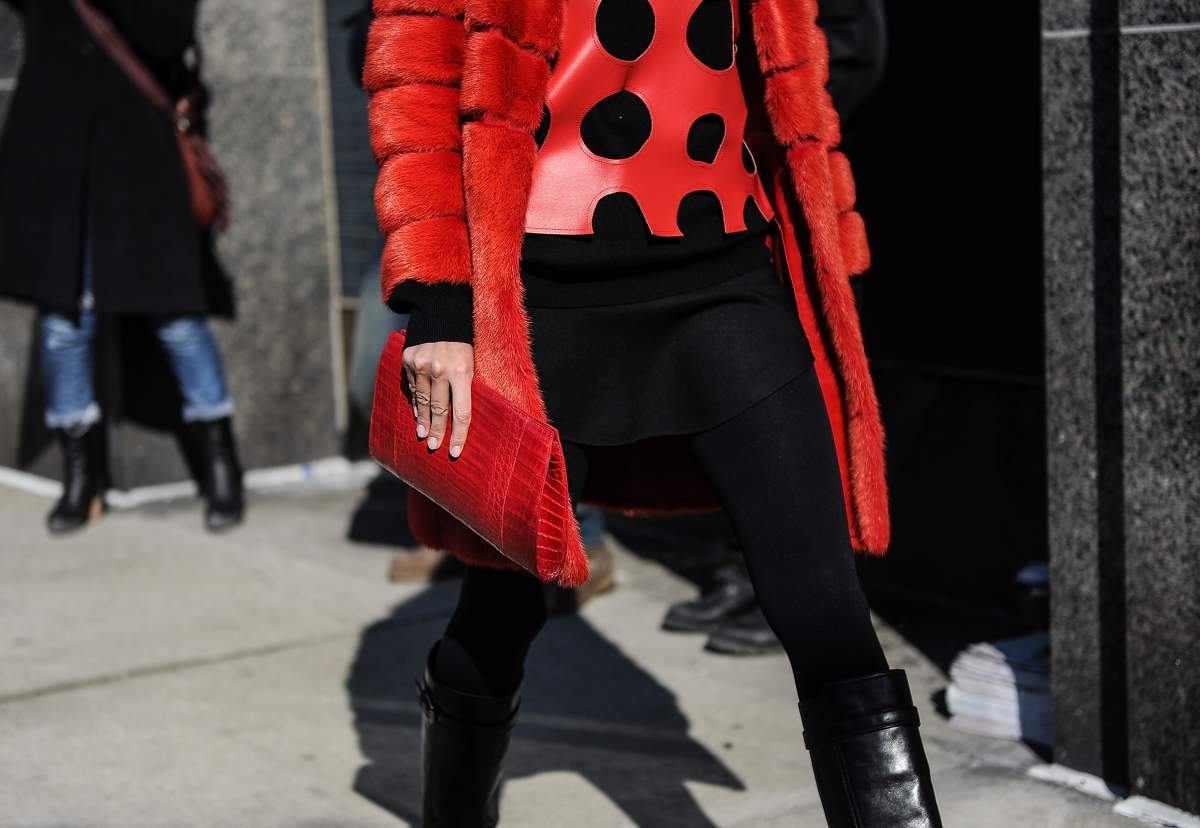 Giovanna Battaglia in a red coat, red and black polka dot top, black trousers. She is carrying a red clutch bag.
