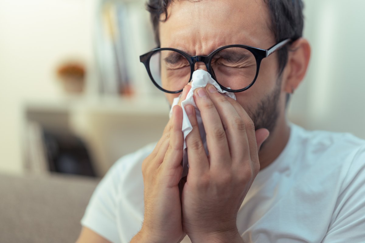 Young man with allergies sneezing, wiping his nose with a piece of tissue paper