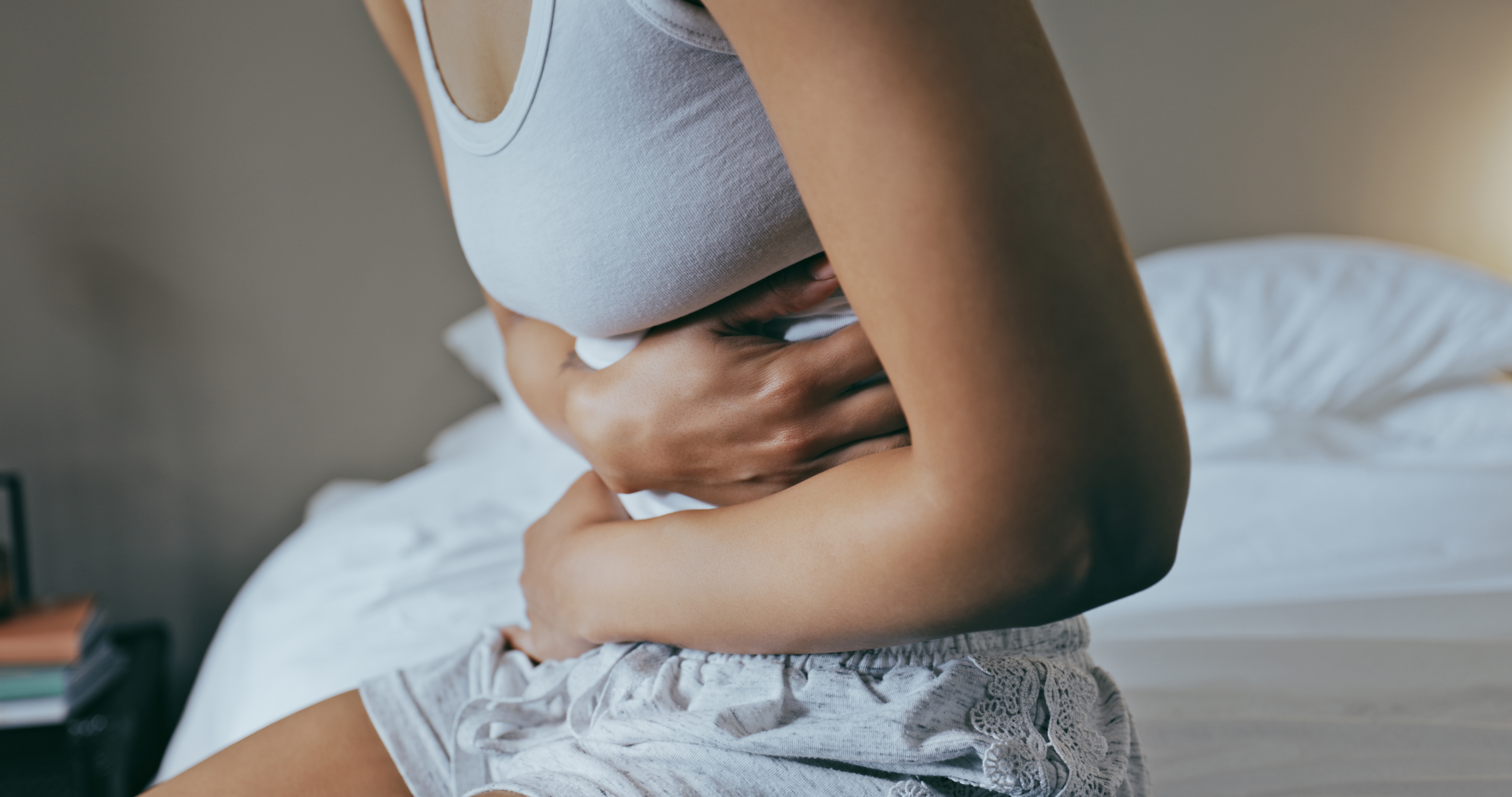 Woman sitting on the edge of her bed and clutching her stomach with discomfort from bloating