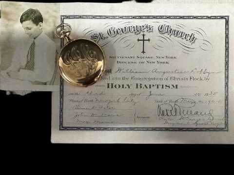A gold pocket watch, closed, lays atop a black and white photo of a boy and a baptismal certificate.