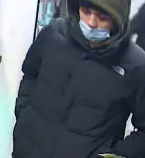The suspect is described as a man in his early 20s wearing a blue medical mask, a dark olive green hoodie with a black 'The North Face' jacket, black pants with stripes on the sides and black runners with white accents.