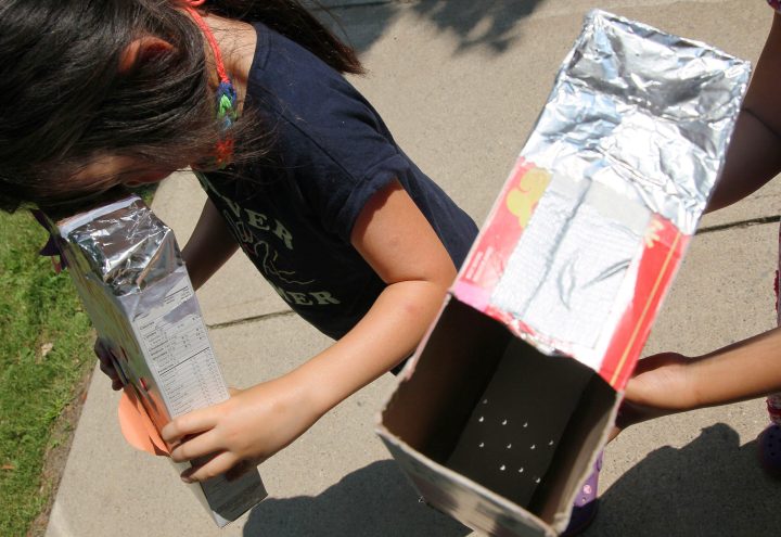 People look through homemade pinhole viewers during a partial solar eclipse