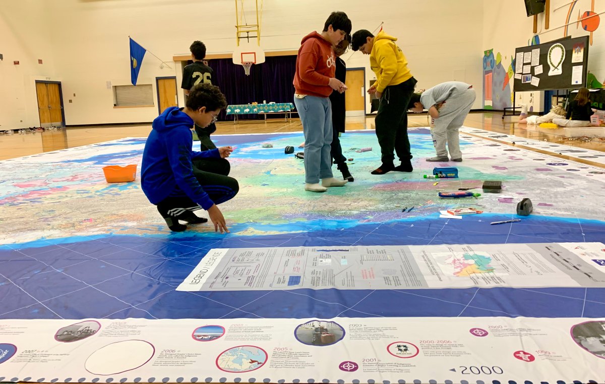 A giant 11 by eight foot map lays across the gym floor of Sweet Grass Elementary School in Edmonton with students crawling all over it.