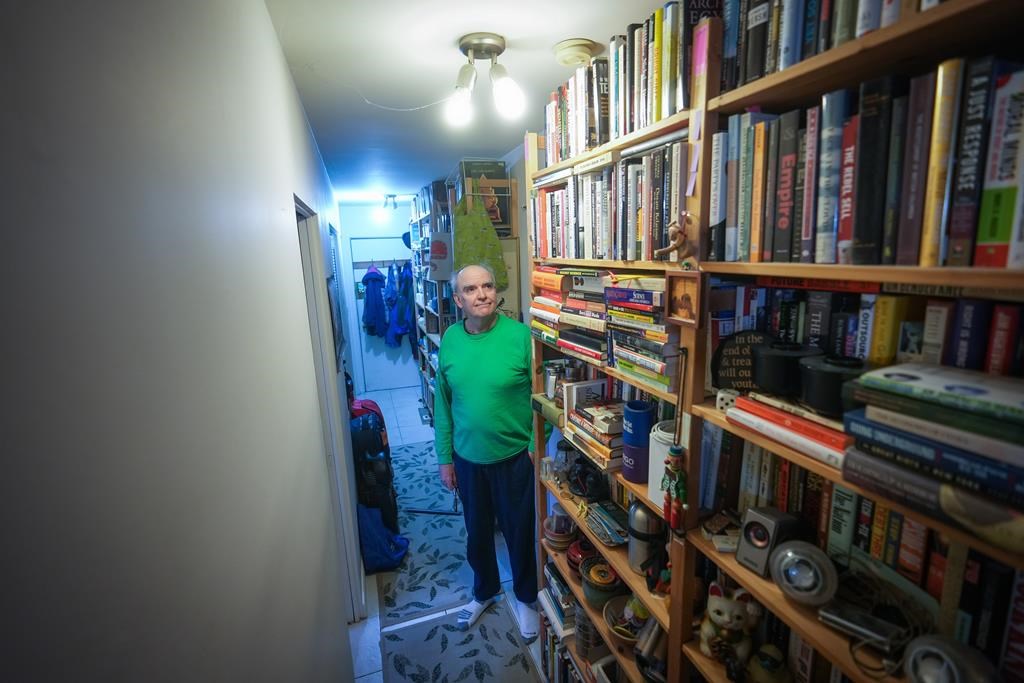 John William, who is losing his sight, poses for a photograph with his collection of books that he has decided to sell, in Vancouver, on Wednesday, April 24, 2024.