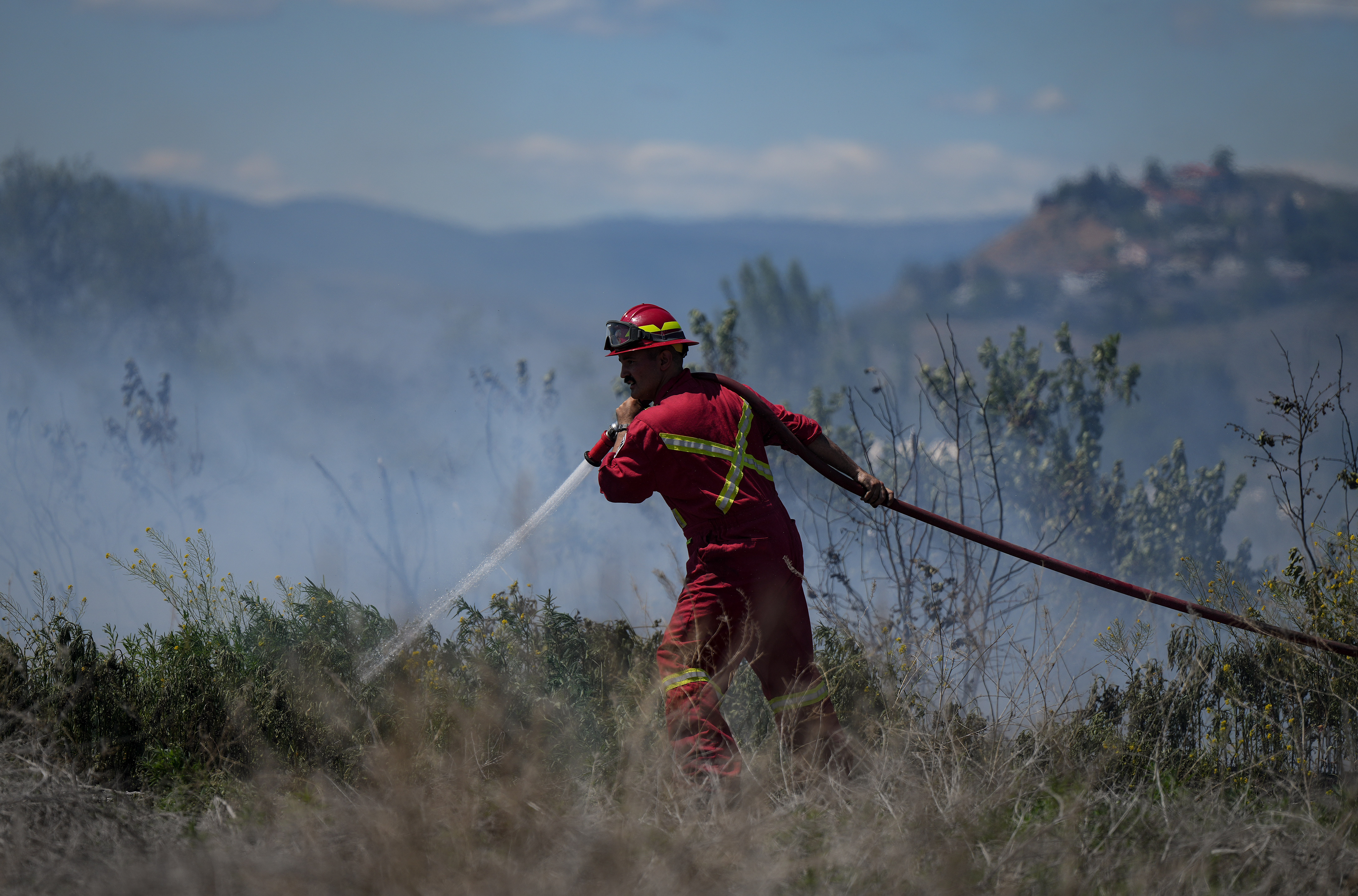A firefighter directs water on a grass fire burning on an acreage behind a residential property in Kamloops, B.C.