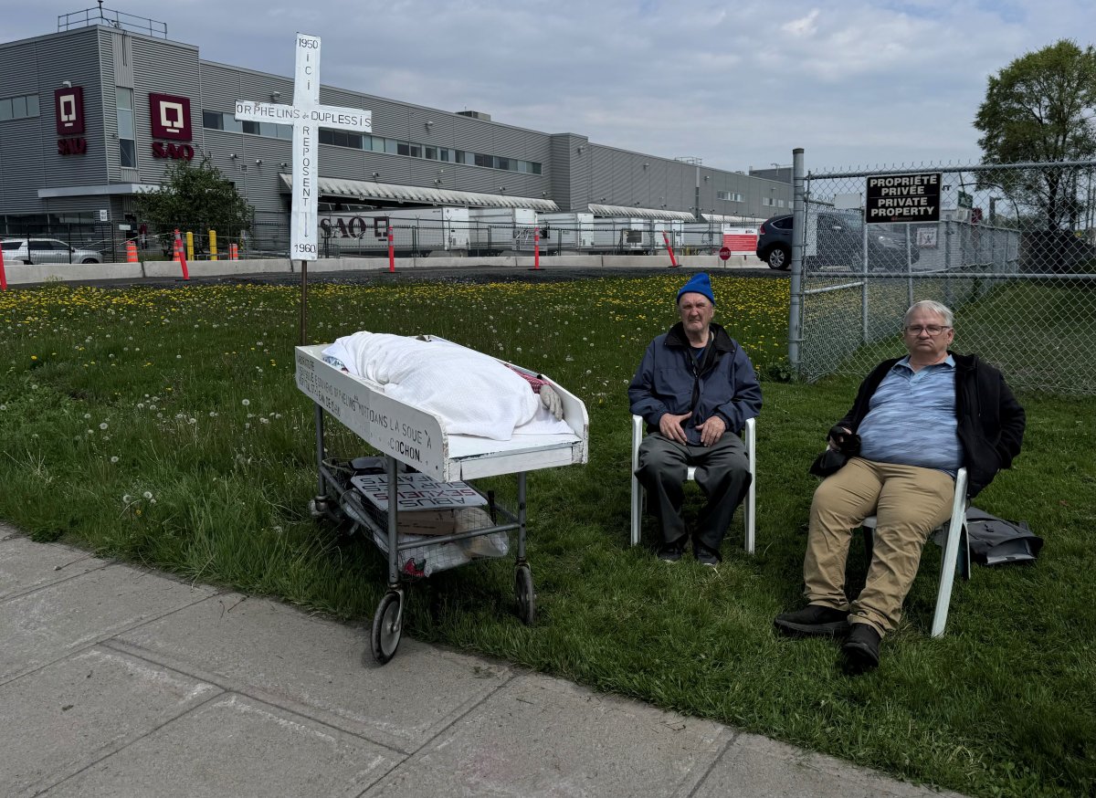 Two representatives of the Duplessis orphans protest outside an SAQ warehouse in the east end of Montreal, Wednesday, May 15, 2024. That group and the Mohawk Mothers want the company to stop work on the building of a new warehouse until cadaver dogs can confirm whether human remains are on the construction site of a new warehouse.