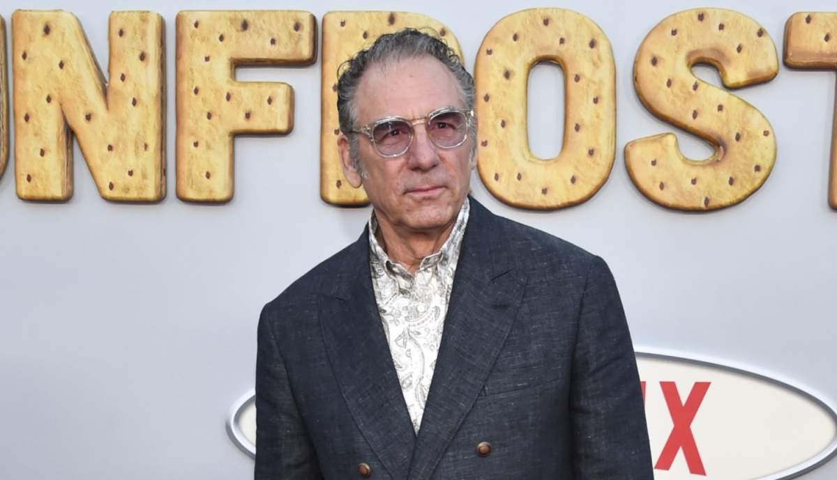 Michael Richards in a blue suit jacket, white shire and sunglasses.