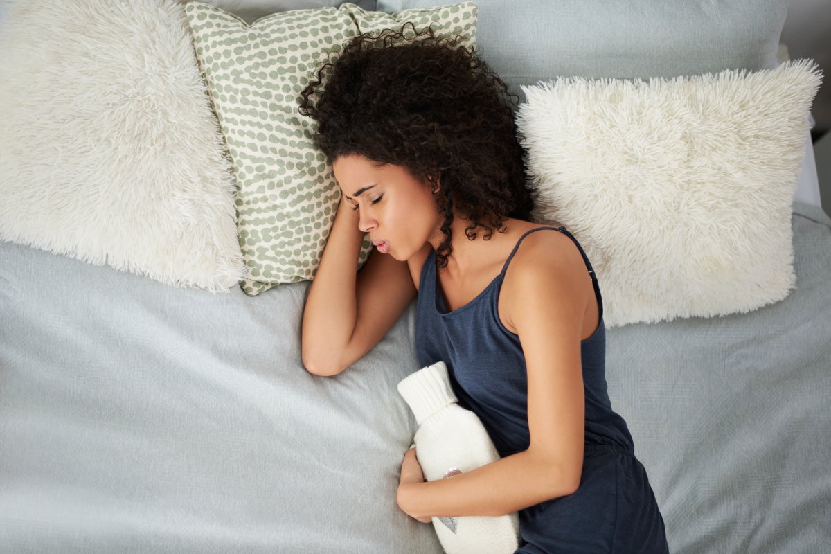 woman suffering from period cramps while lying in bed with a hot water bottle