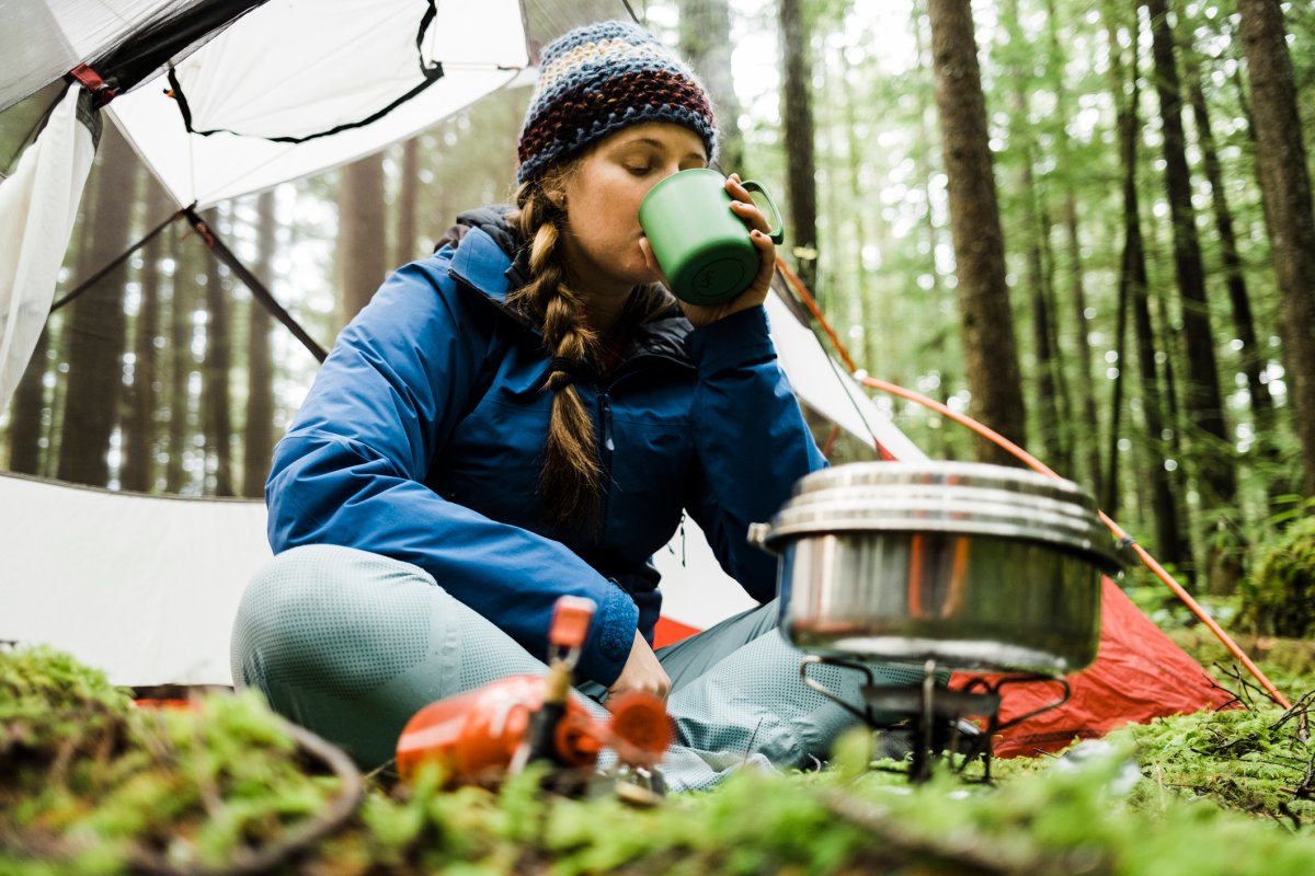 Woman at a camp site drinking a cup of coffee in front of a fire