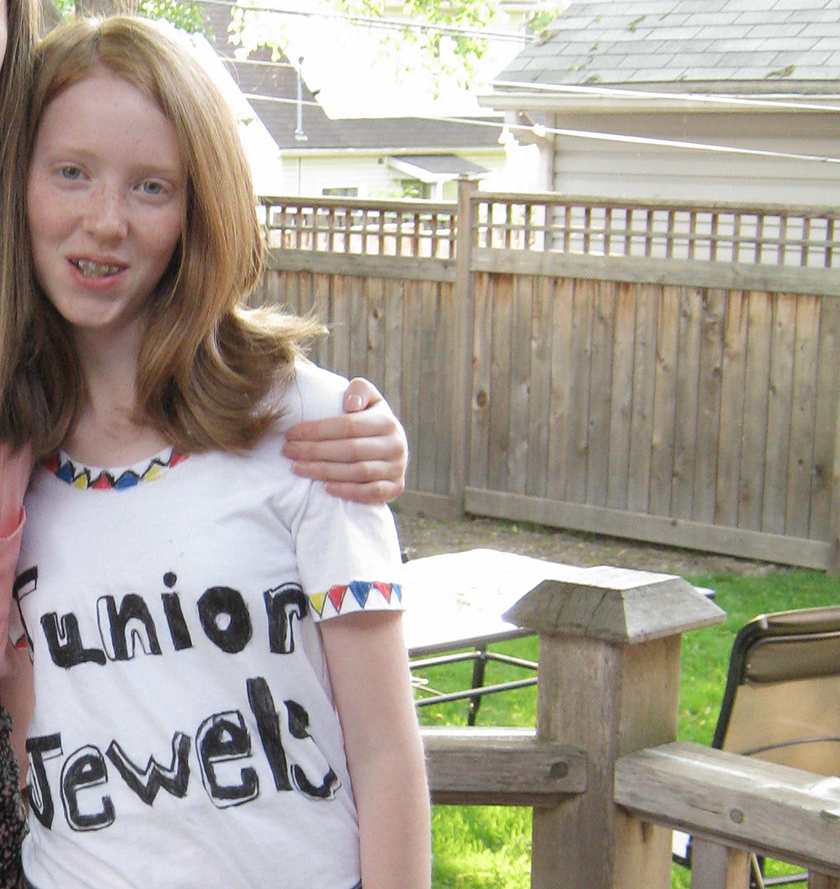 Meghan Nolan in a homemade 'Junior Jewels' tee. She is standing in a fenced yard.