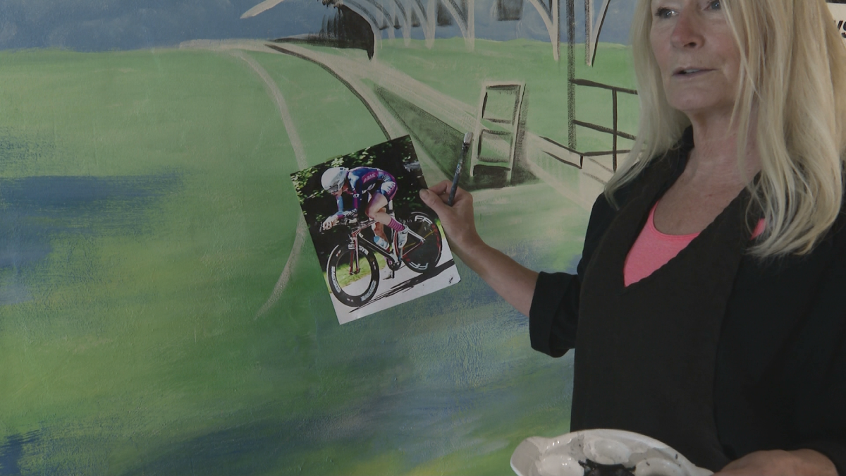 Hill is holding a photo of Ellen Watters who will be featured in the mural.