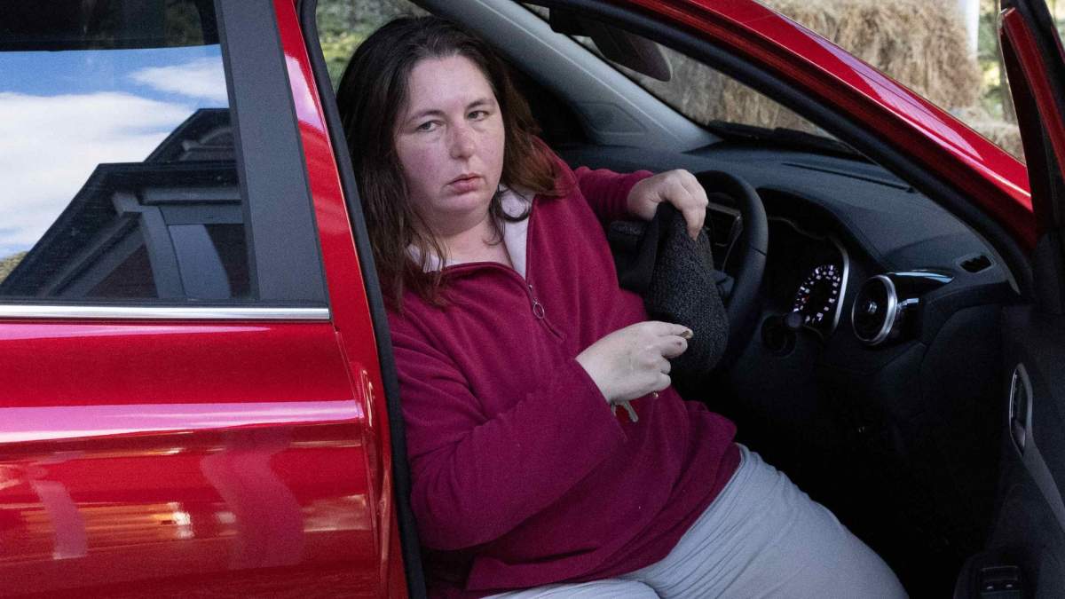 Erin Patterson in a red car. She is wearing a red sweater and stepping out of the open driver's side door.