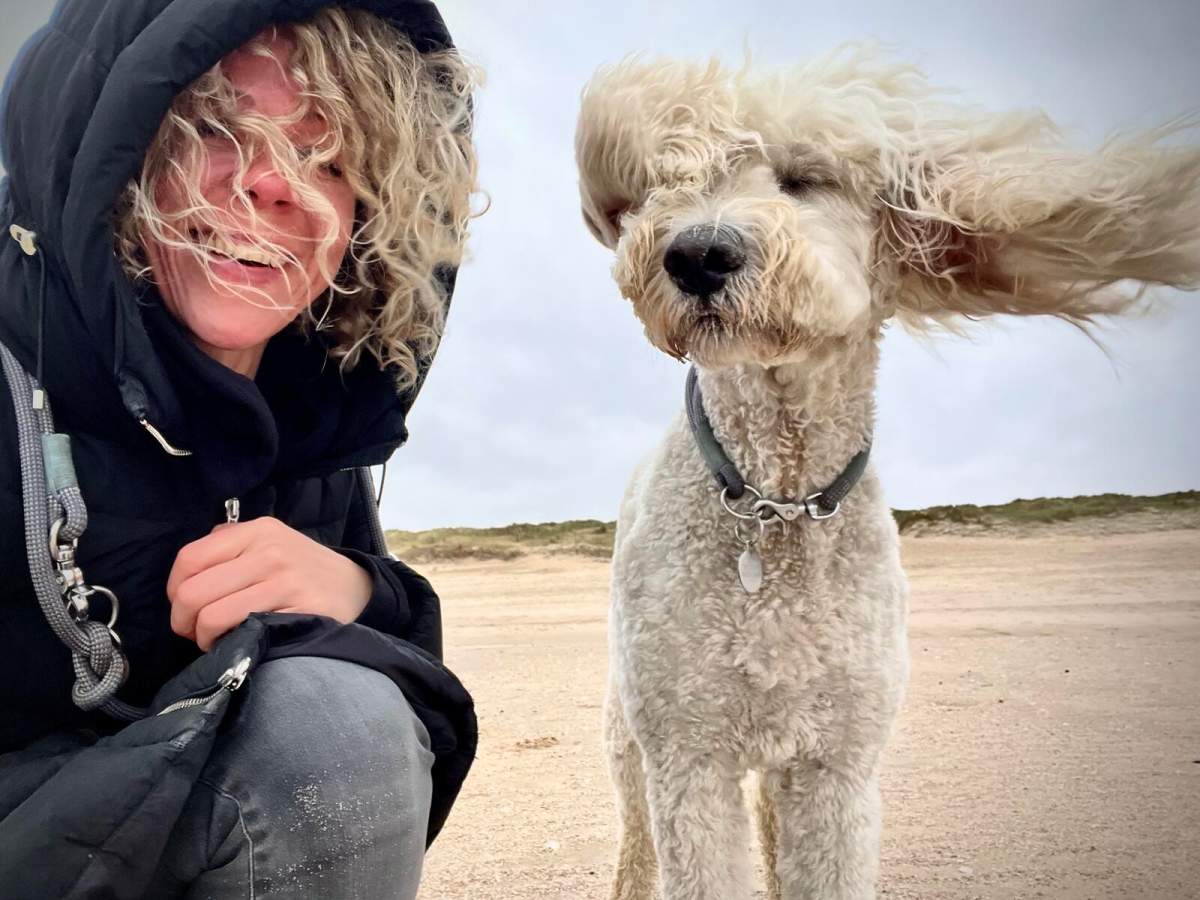 A woman with curly hair next to her dog, who also has curly hair.
