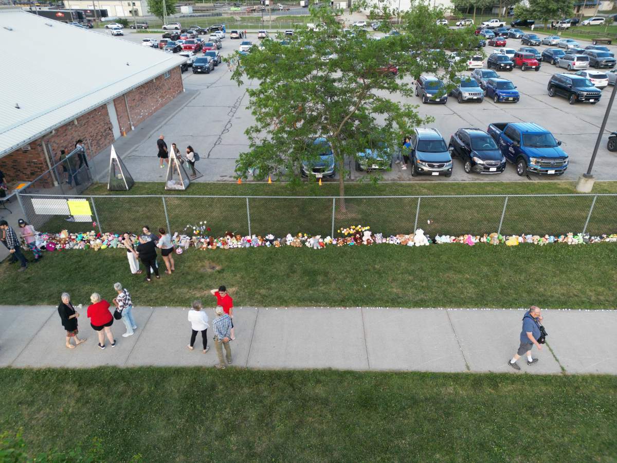 Stuffed animals and flowers line a fence in an aerial shot.