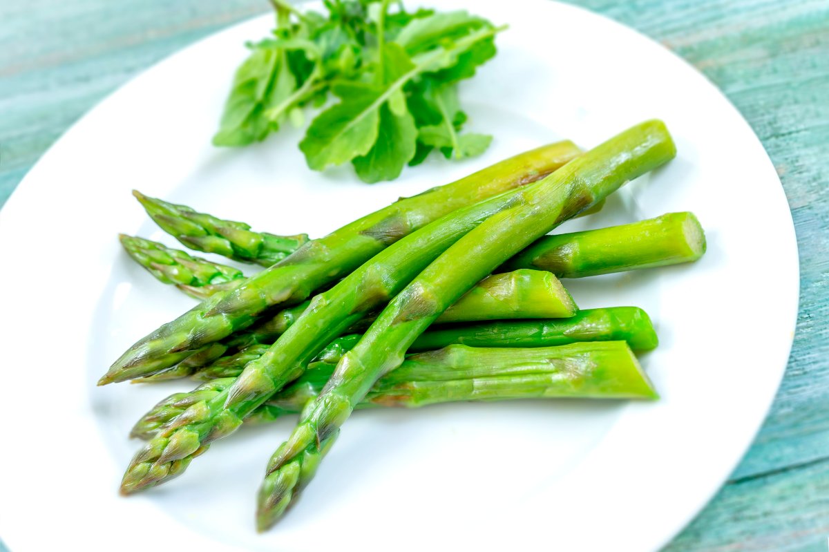 Close-up of cooked asparagus on the plate on a green wooden table.