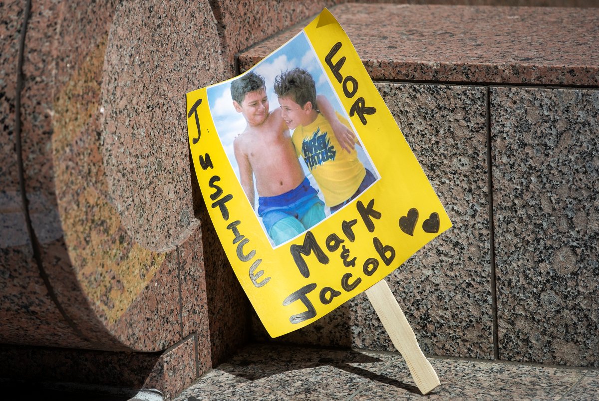 A yellow sign with a photo of two boys in swimsuits. Their arms are around one another. One boy wears a yellow tee, the other does not wear one at all. The sign in black marker reads, "Justice for Mark and Jacob."