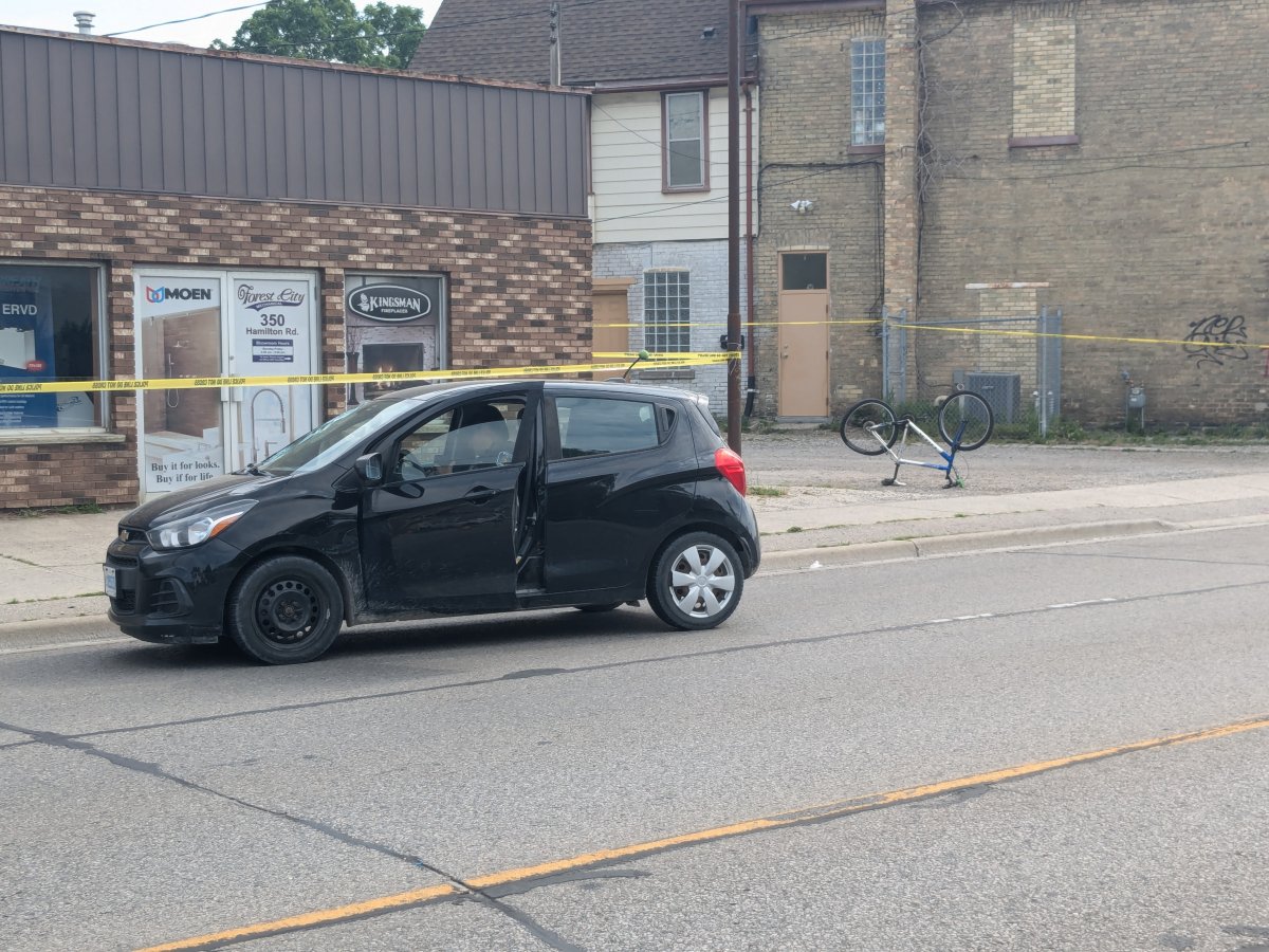 A black vehicle in front of police caution tape and a one story commercial building in the daytime.