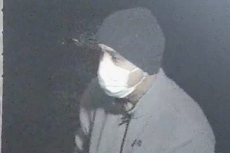 A surveillance photo of a man in a mask and dark-coloured clothing.