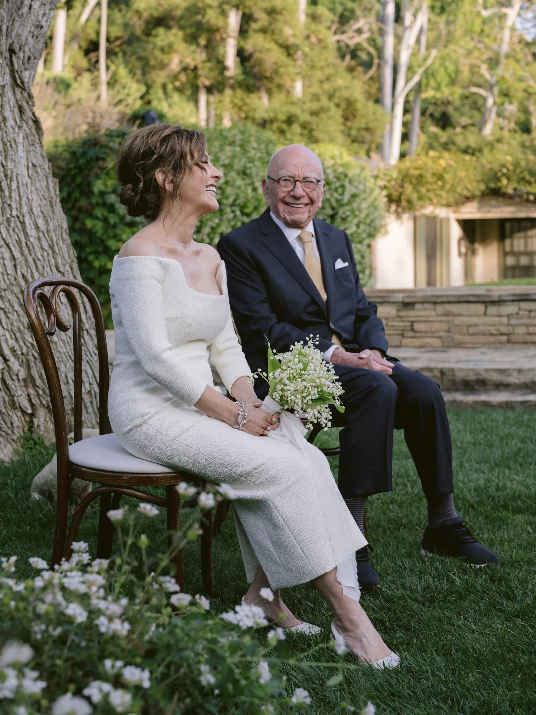 Elena Zhukova and Rupert Murdoch sitting in their wedding attire. She is holding a white bouquet.