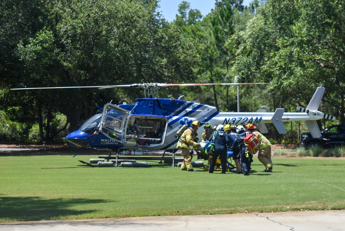 Firefighters and others carry a stretcher to a blue helicopter on the grass.