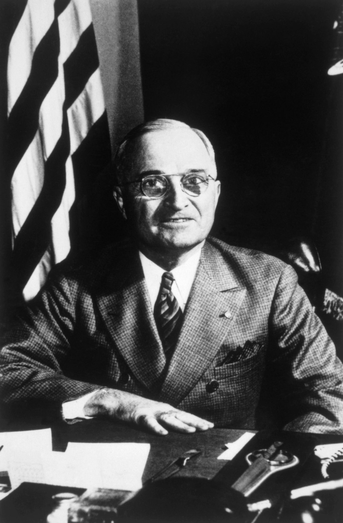 U.S. President Harry S. Truman sits in front of U.S. flag.