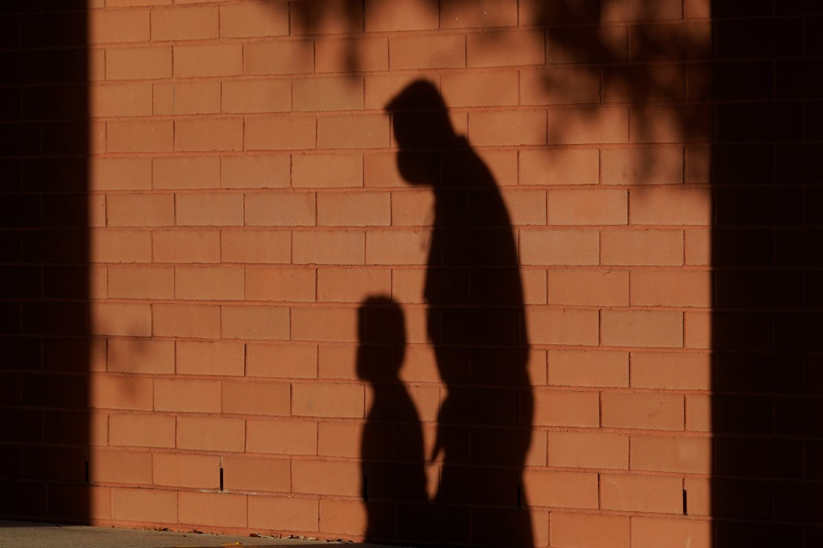 The shadow of a school employee escorting a student is cast on the wall as they walk to a classroom.