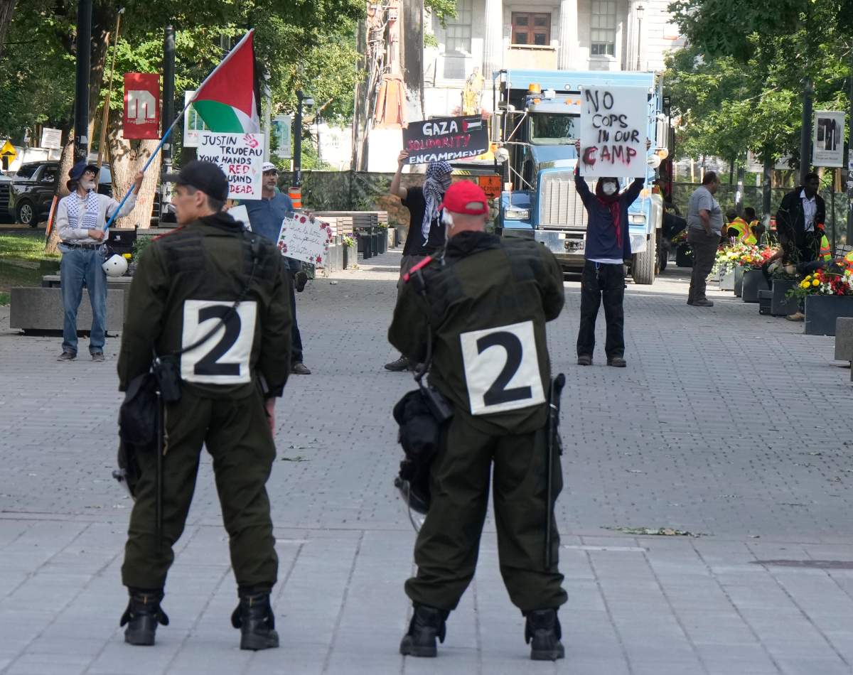 Police stand by as protesters holds up signs at McGill University in Montreal, Wednesday, July 10, 2024. The university closed its downtown campus as police descended in large numbers to help clear a pro-Palestinian encampment.