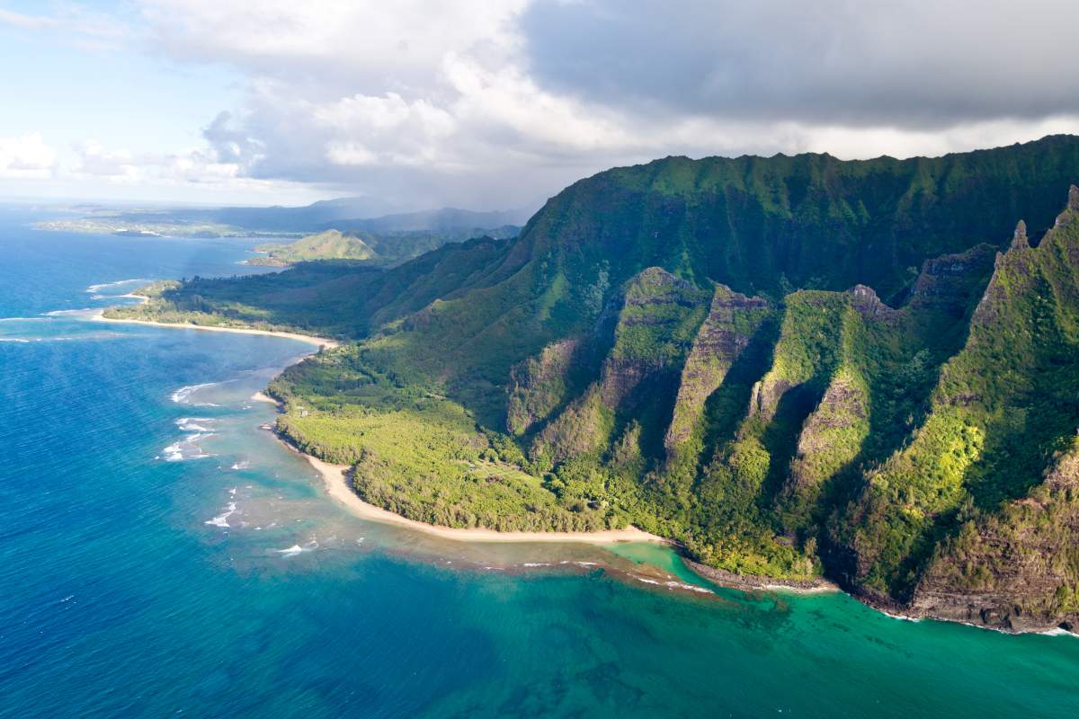 An aerial shot of the Na Pali Coast on the island of Kaua'i showing blue water and lush, green mountains.