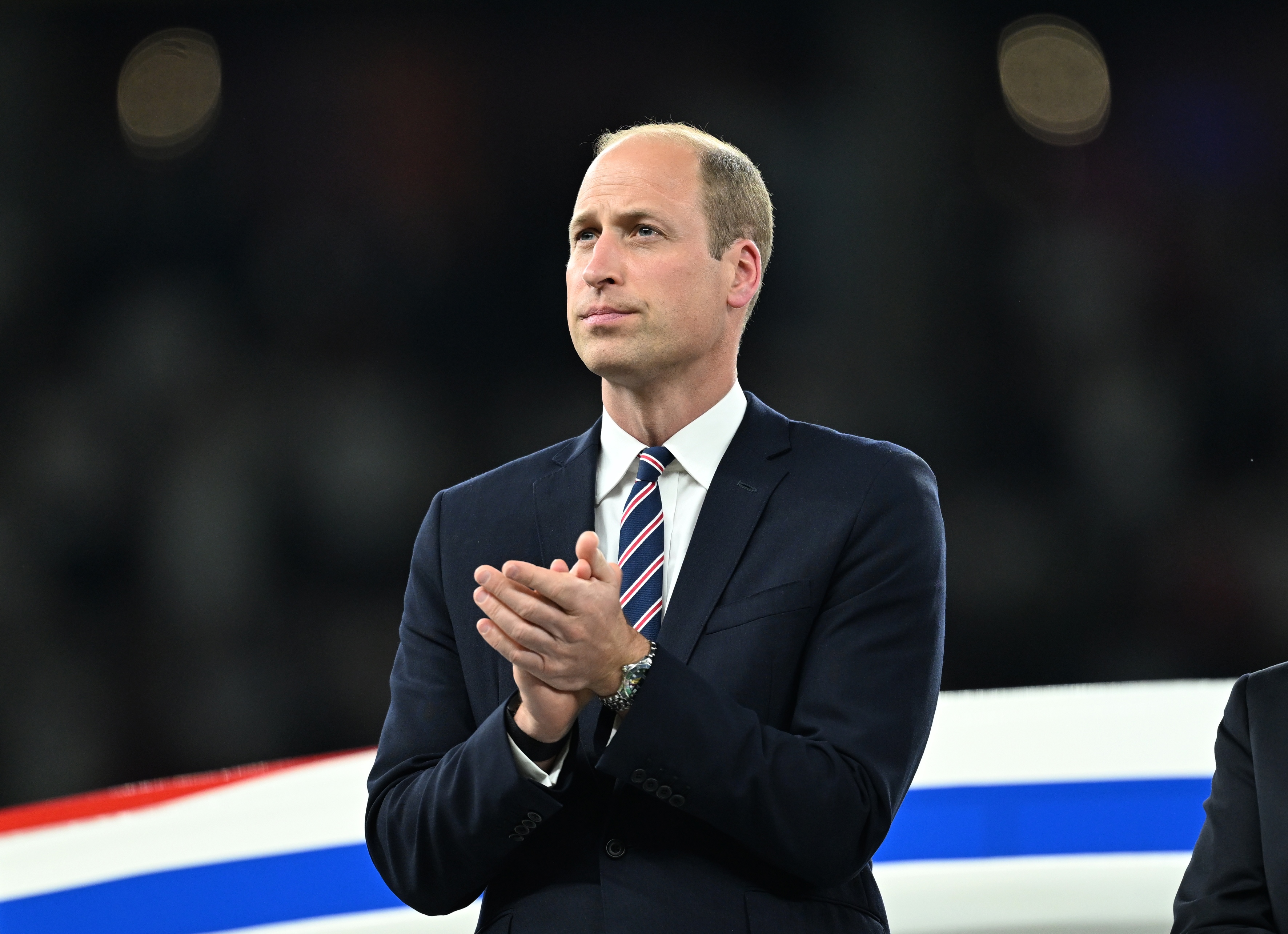 Prince William clapping in a black suit.