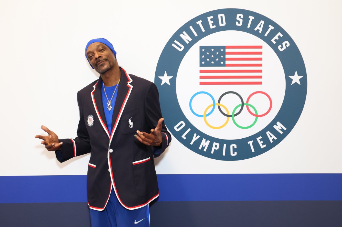 Snoop Dogg poses in a polo jacket in front of a sign that reads "United States Olympic Team."
