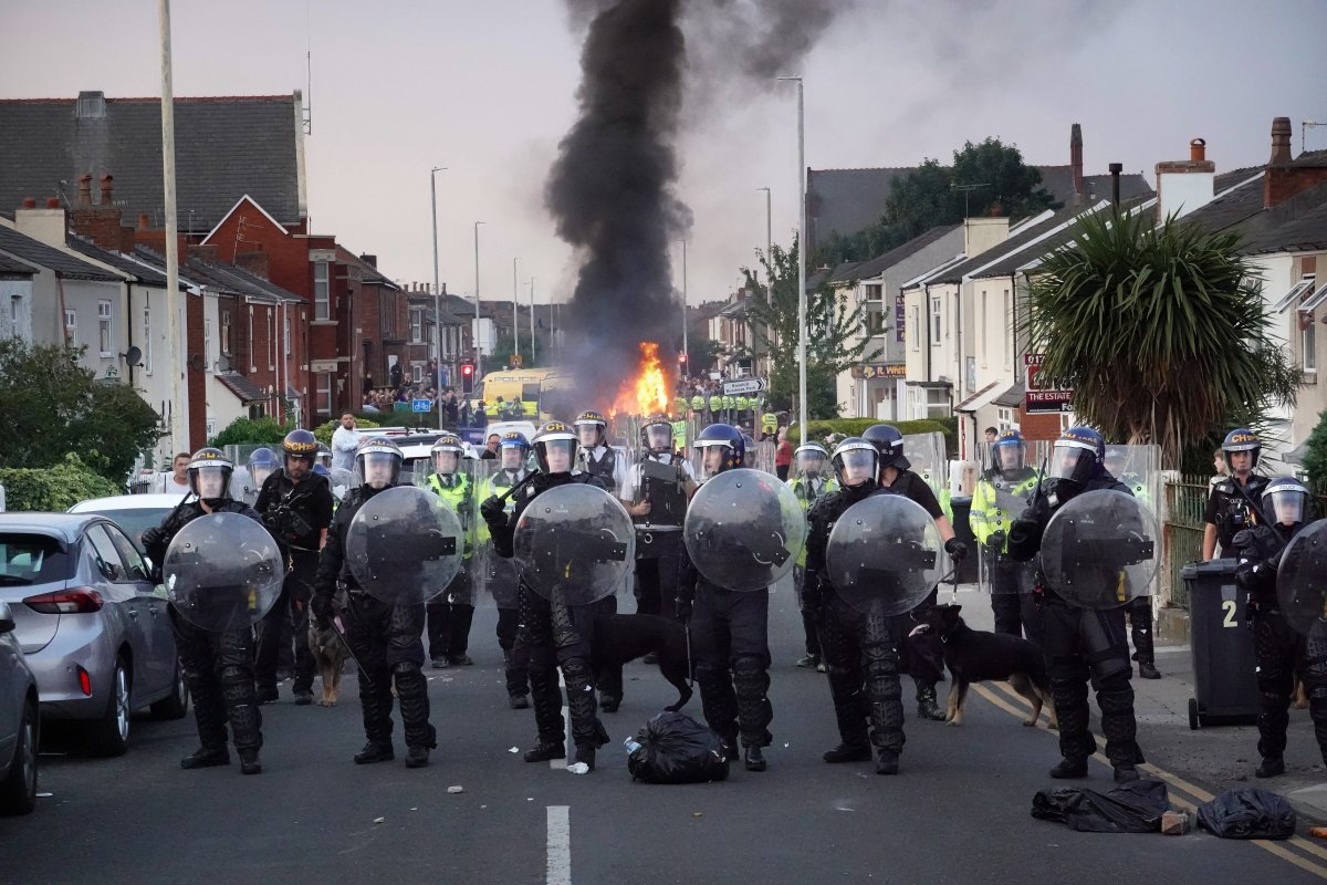 Riot police hold back protesters near a burning police vehicle after disorder broke out on July 30, 2024 in Southport, England.