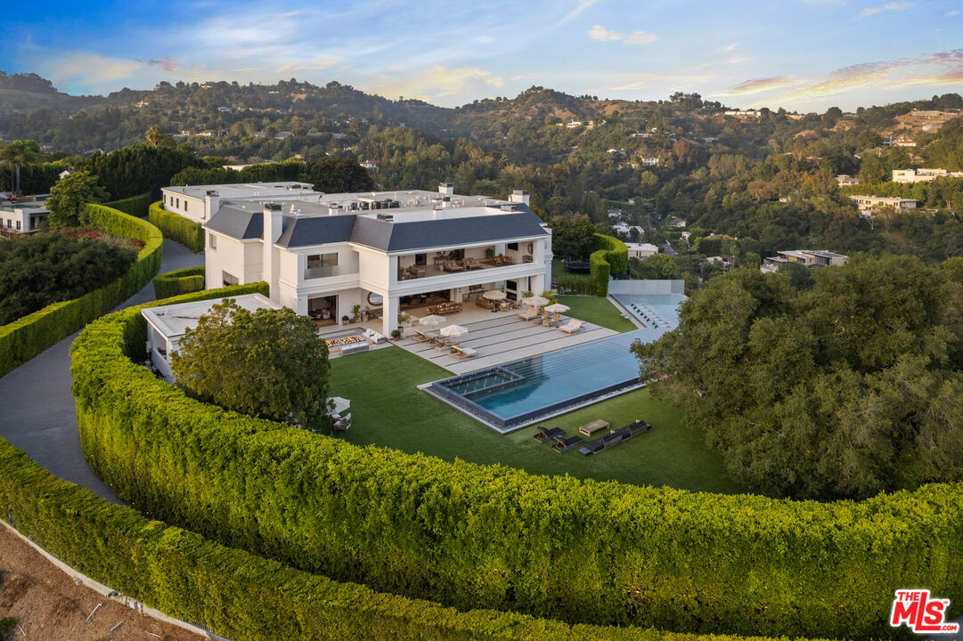 Aerial view of the mansion, showing a large backyard and pool enclosed behind tall hedges.