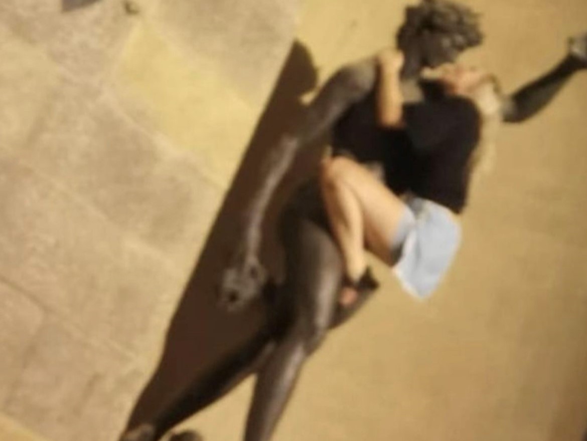 A blurry photo of a woman with her leg up on a statue of Bacchus. Her arms are around the statue's neck as she leans in for a mock kiss.