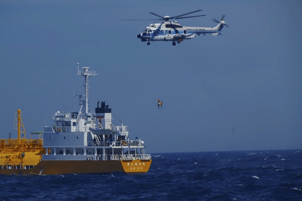 A ship and a helicopter. The helicopter is lifting a figure from the ship by a rope.