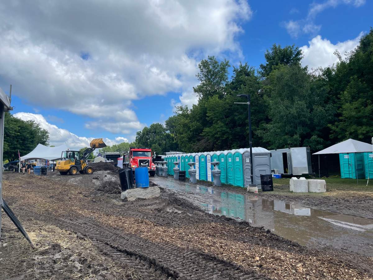 A row of portable toilets behind a wet, muddy ground.