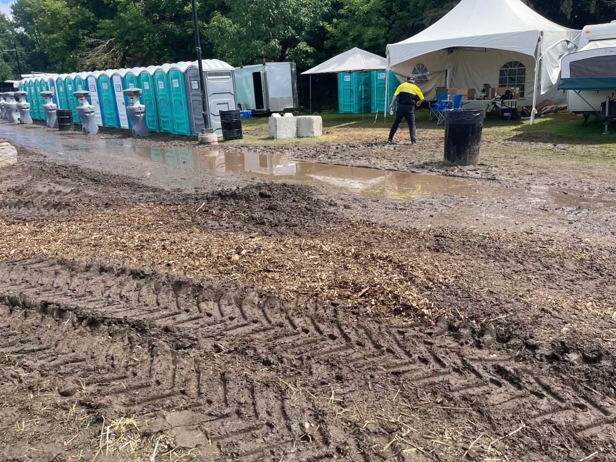 Mud in front of a muddy puddle and portable toilets in a park.