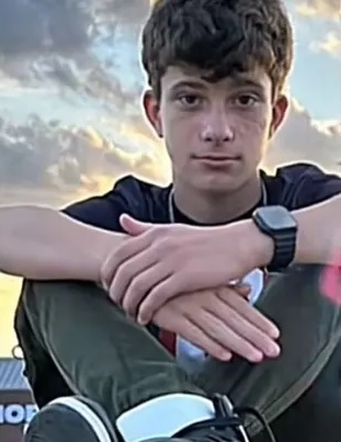 A photo of a teenage boy sitting in front of a cloudy sky.