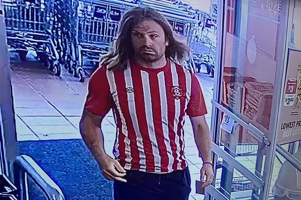 A surveillance photo of a man in a red and white striped soccer jersey in front of grocery carts.