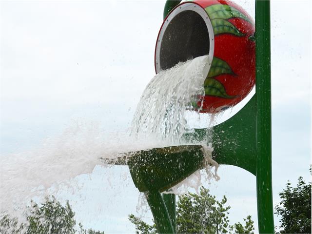 A bucket in the shape of a tomato spilling water at a splash pad.