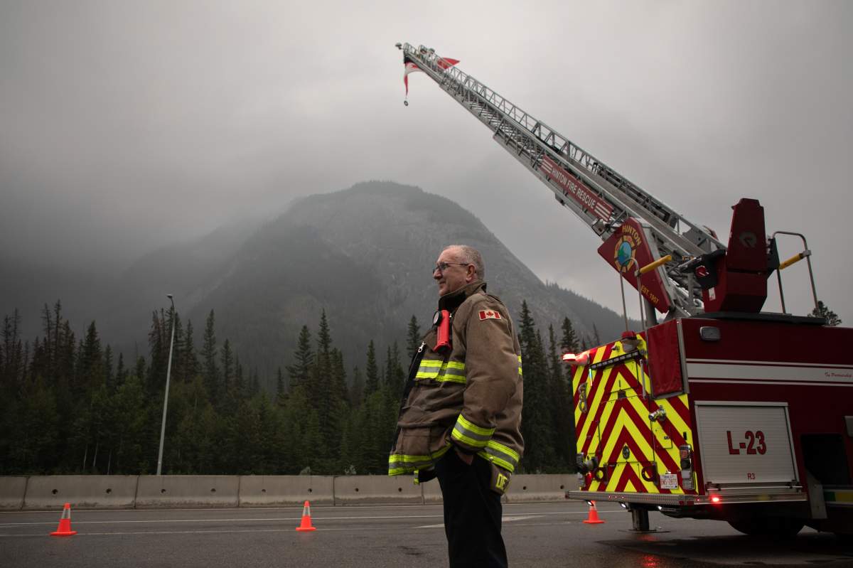 Hinton Fire Chief Mac de Beaudrap waits at the Park Gate with a Canadian flag to greet returning residents to Jasper, Alberta on Friday August 16, 2024. Wildfire caused evacuations and widespread damage in the National Park and Jasper townsite. THE CANADIAN PRESS/Police and Park rangers wait for residents at the park gates on the first day residents are able to visit their Jasper, Alberta, properties on Friday August 16, 2024. Wildfire caused evacuations and widespread damage in the National Park and Jasper townsite.