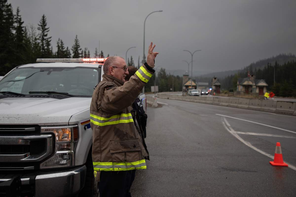 Hinton Fire Chief Mac de Beaudrap and an RCMP officer wave in greeting to returning residents to Jasper, Alberta on Friday August 16, 2024. Wildfire caused evacuations and widespread damage in the National Park and Jasper townsite.