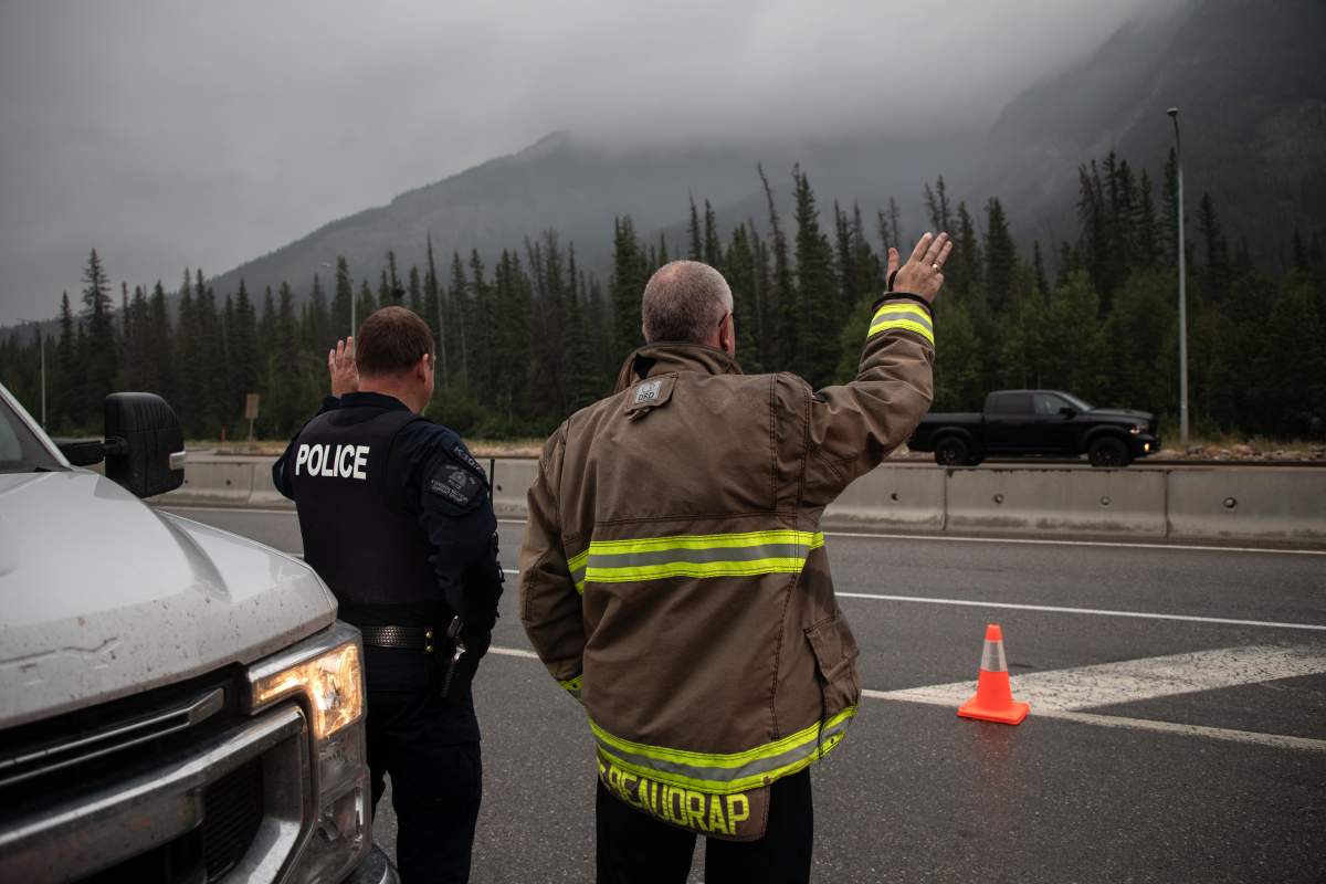 Hinton Fire Chief Mac de Beaudrap and an RCMP officer wave in greeting to returning residents to Jasper, Alberta on Friday August 16, 2024. Wildfire caused evacuations and widespread damage in the National Park and Jasper townsite.