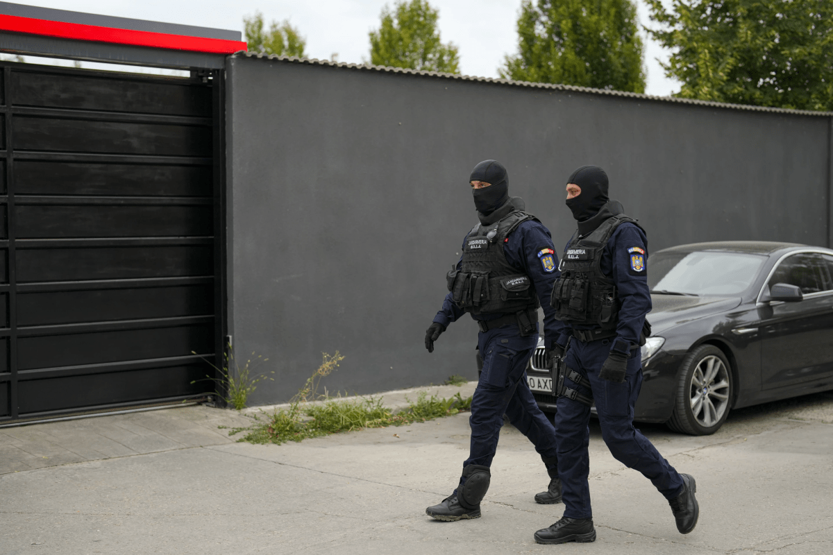 Two masked guards walk alongside a wall.