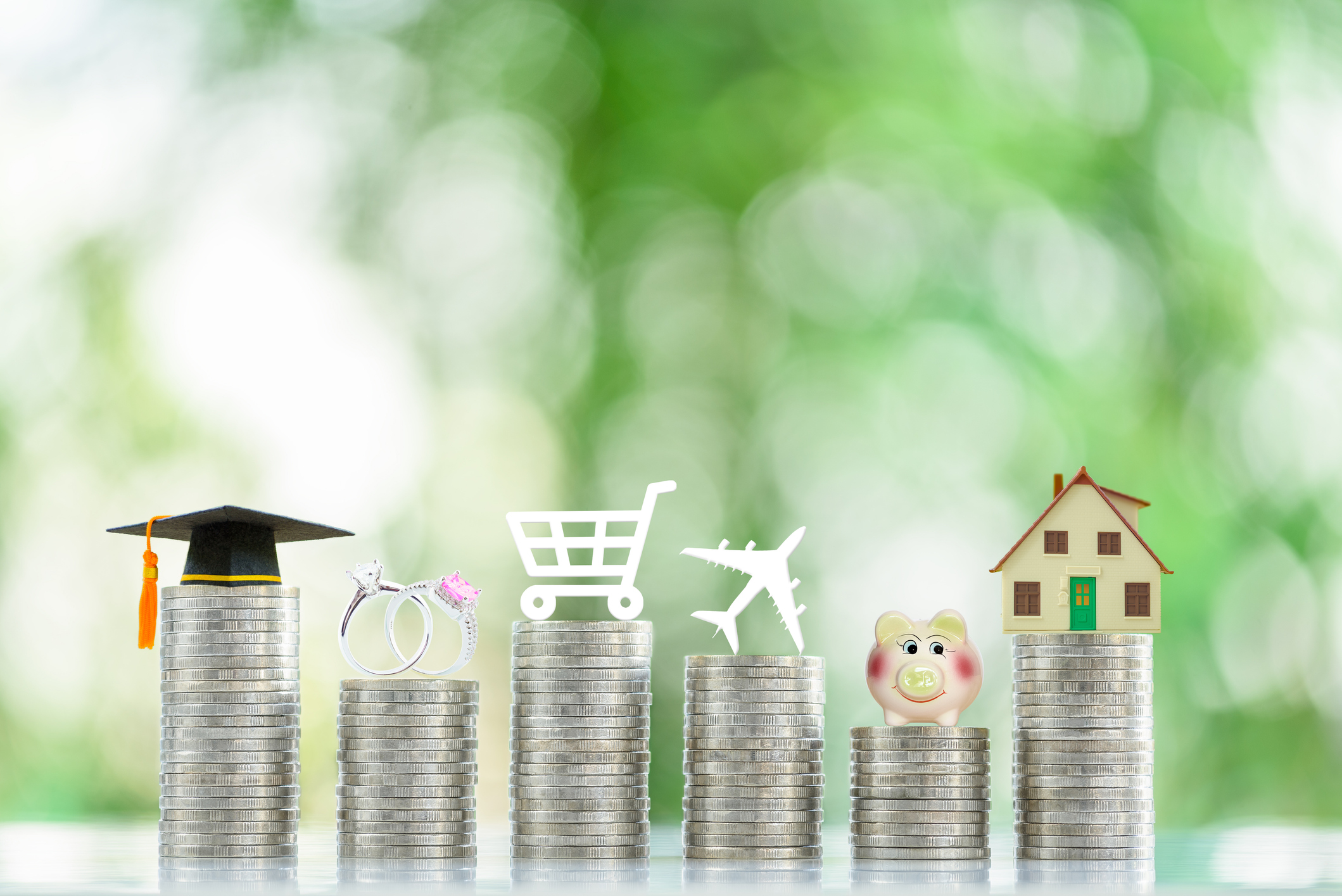 Personal expense and weekly budget, financial concept : Six coin stacks with logos on top e.g a black graduation cap, a wedding or engagement rings, a shopping cart, a house, a plane, a piggy bank.