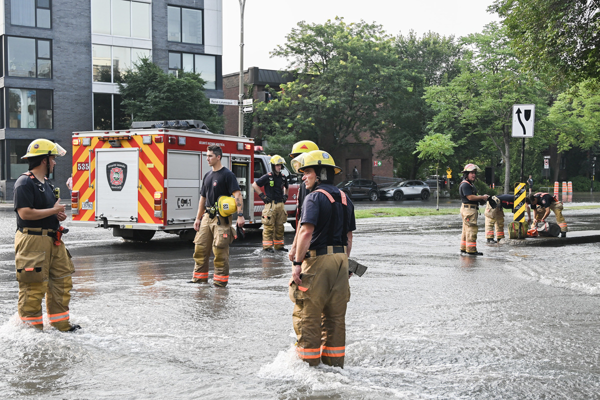 Firefighters survey the scene after a watermain break on a street in Montreal, Friday, August 16, 2024, causing flooding in several streets of the area.