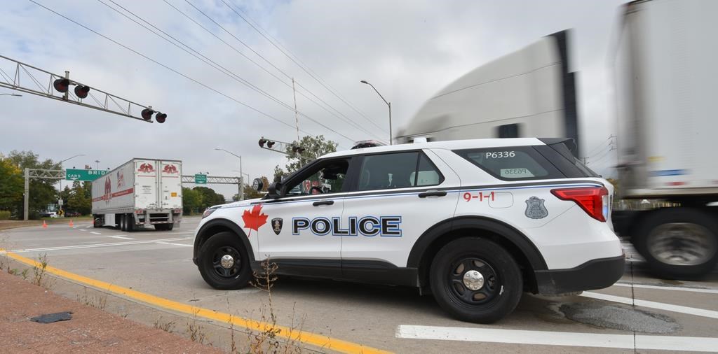 A police vehicle is on the scene as trucks make their way to the Ambassador Bridge border crossing in Windsor, Ont., Monday, Oct.4, 2021. Ontario's police watchdog is investigating after a 57-year-old man was fatally shot by a Windsor police officer on Friday.